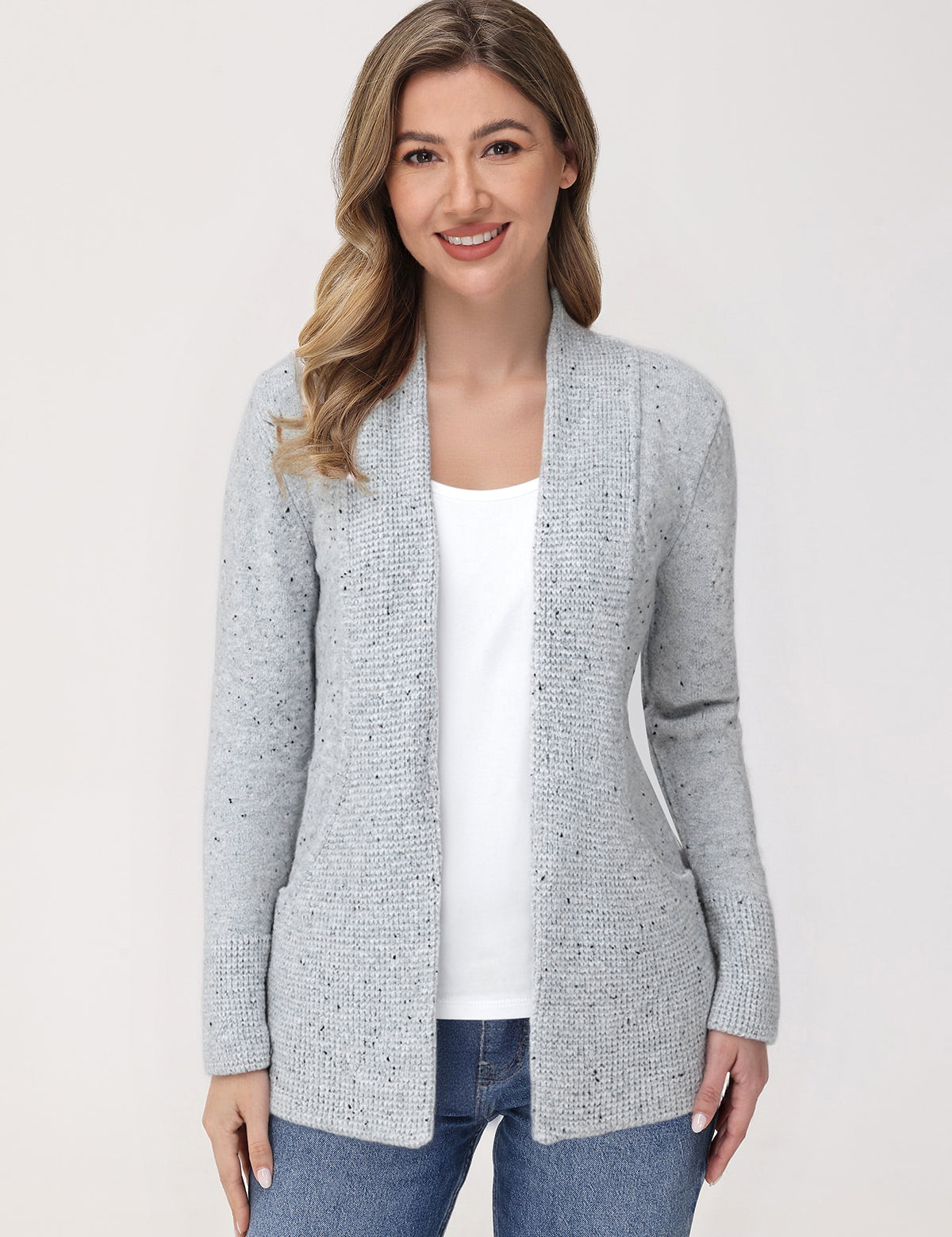 Woman wearing a gray cardigan over a white shirt and blue jeans on a light background