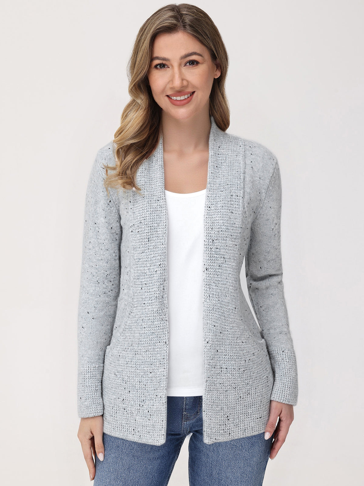 Woman wearing a gray cardigan over a white shirt and blue jeans on a light background