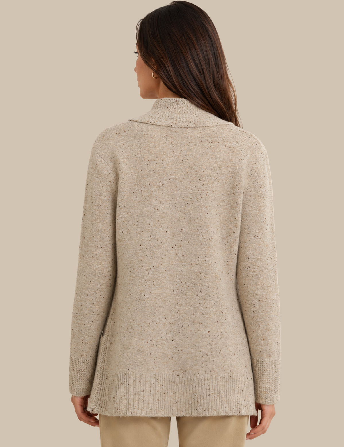 A woman shown from the back wearing a light beige knit sweater with subtle dark flecks, paired with beige pants, against a solid beige background.