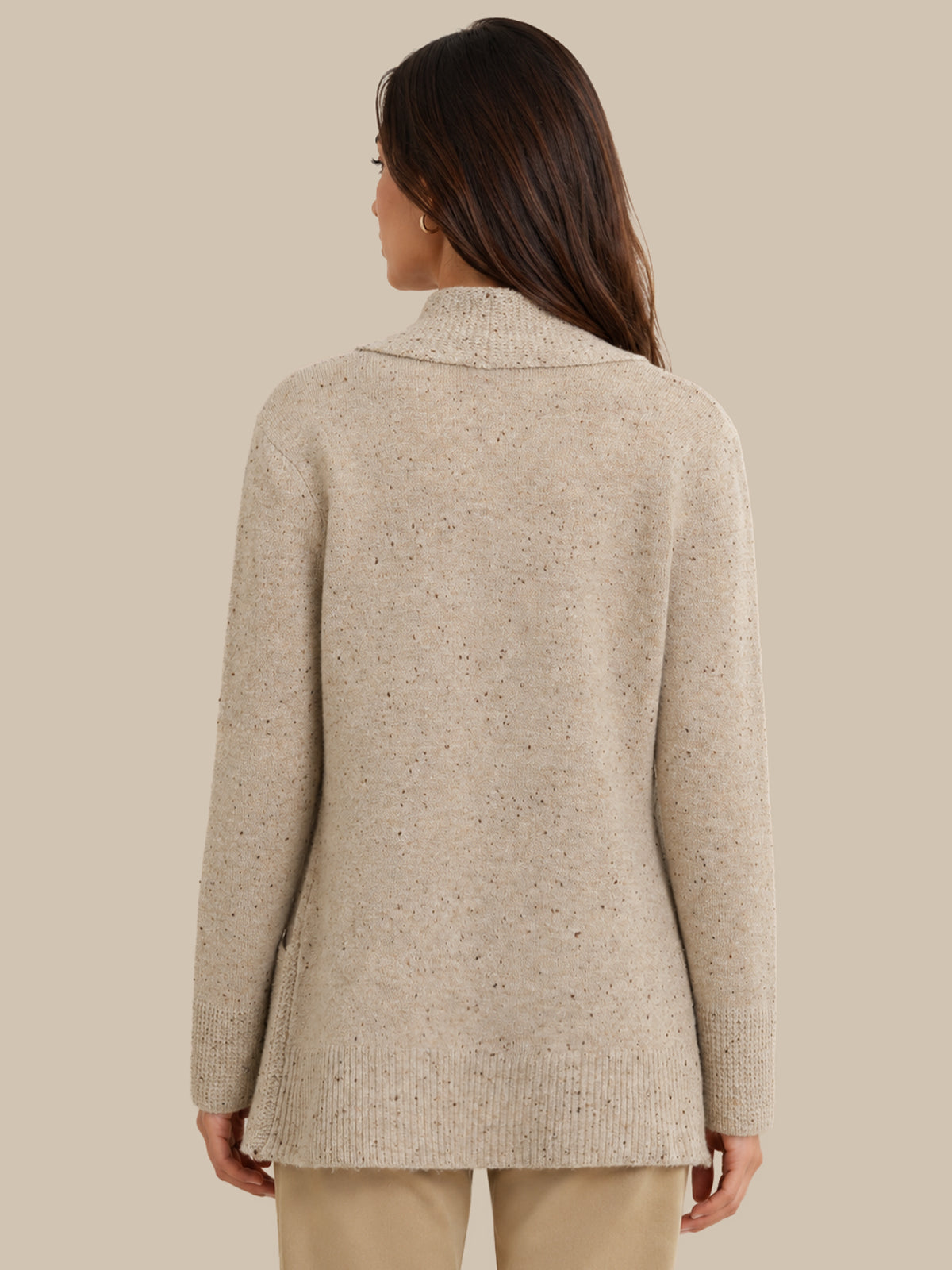 A woman shown from the back wearing a light beige knit sweater with subtle dark flecks, paired with beige pants, against a solid beige background.