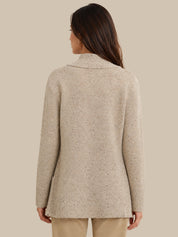 A woman shown from the back wearing a light beige knit sweater with subtle dark flecks, paired with beige pants, against a solid beige background.