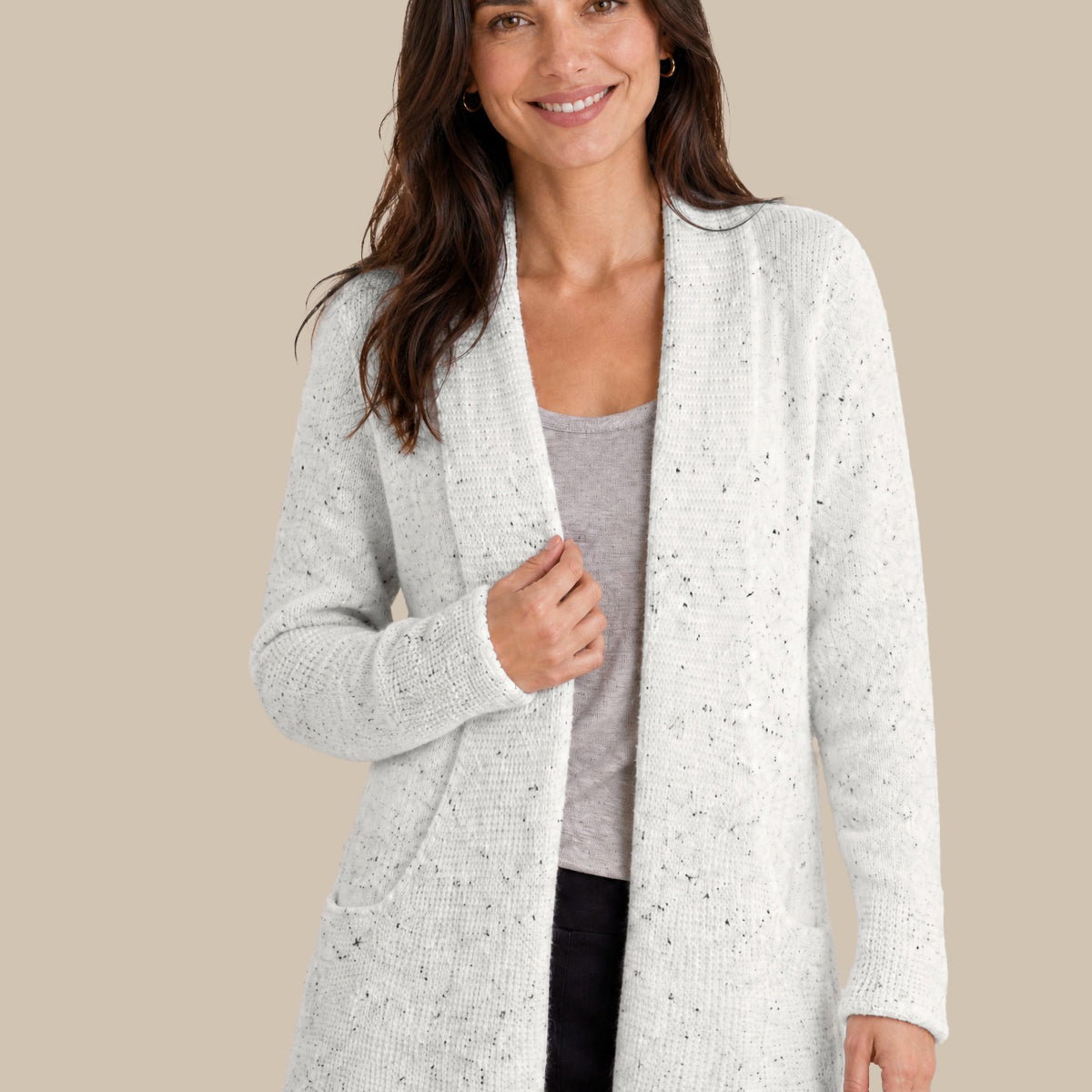 A woman modeling a light white open-front cardigan with subtle black speckles, worn over a gray top and black pants, against a solid beige background.