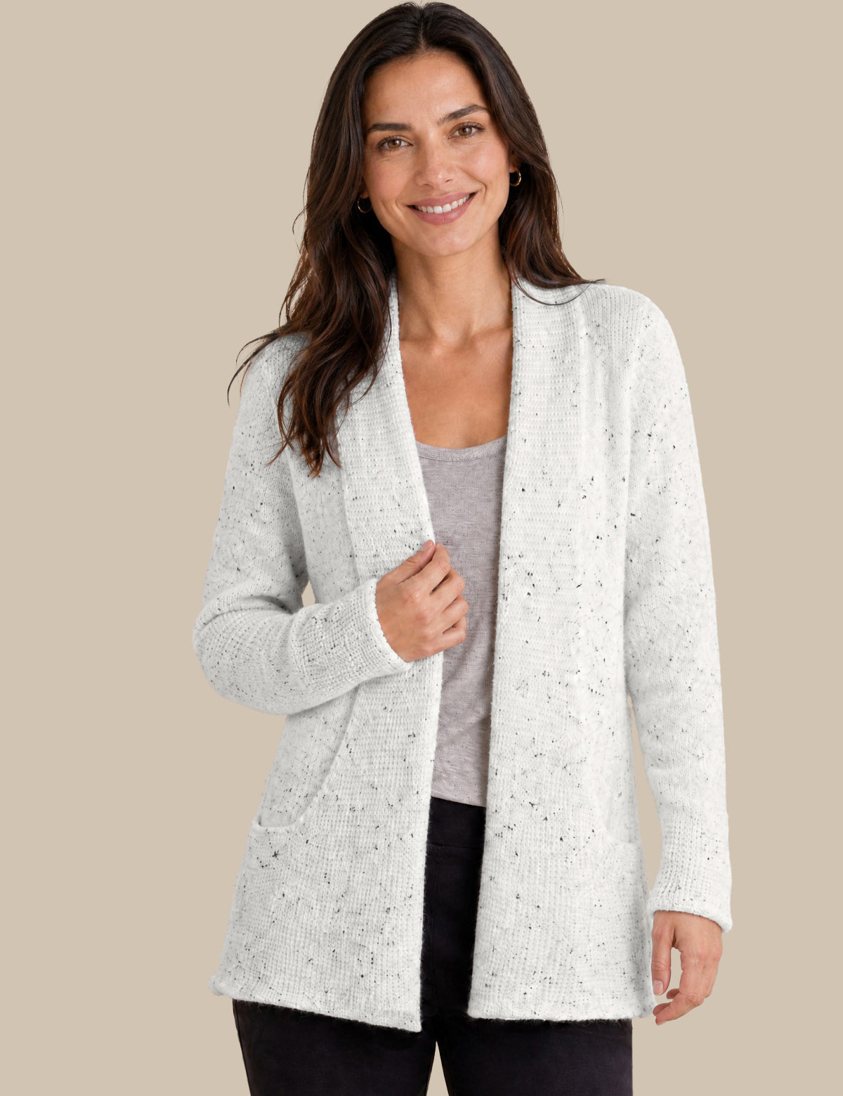 A woman modeling a light white open-front cardigan with subtle black speckles, worn over a gray top and black pants, against a solid beige background.