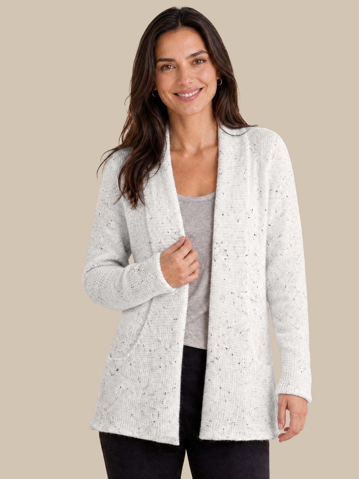 A woman modeling a light white open-front cardigan with subtle black speckles, worn over a gray top and black pants, against a solid beige background.