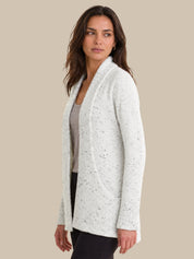 A woman modeling a white open-front cardigan with subtle black speckles, worn over a gray top and black pants, set against a solid beige background.