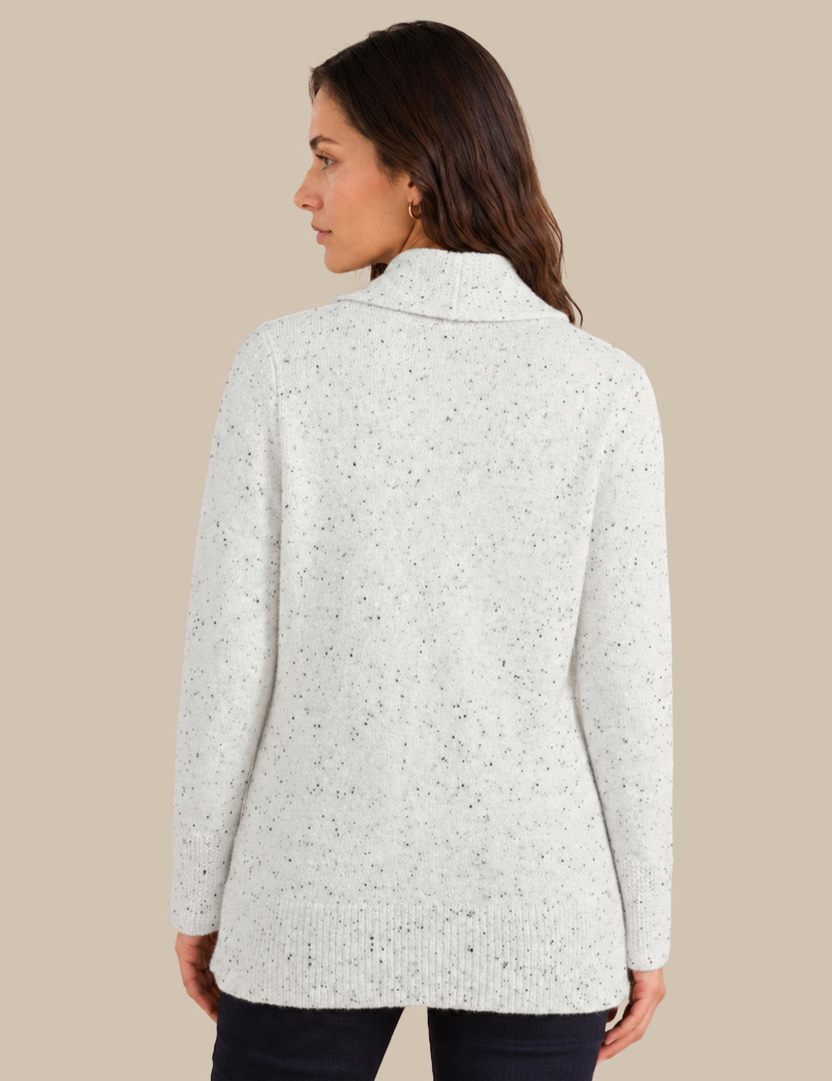 A woman shown from the back wearing a light heathered off-white knit sweater with subtle dark speckles, paired with dark pants, against a solid beige background.