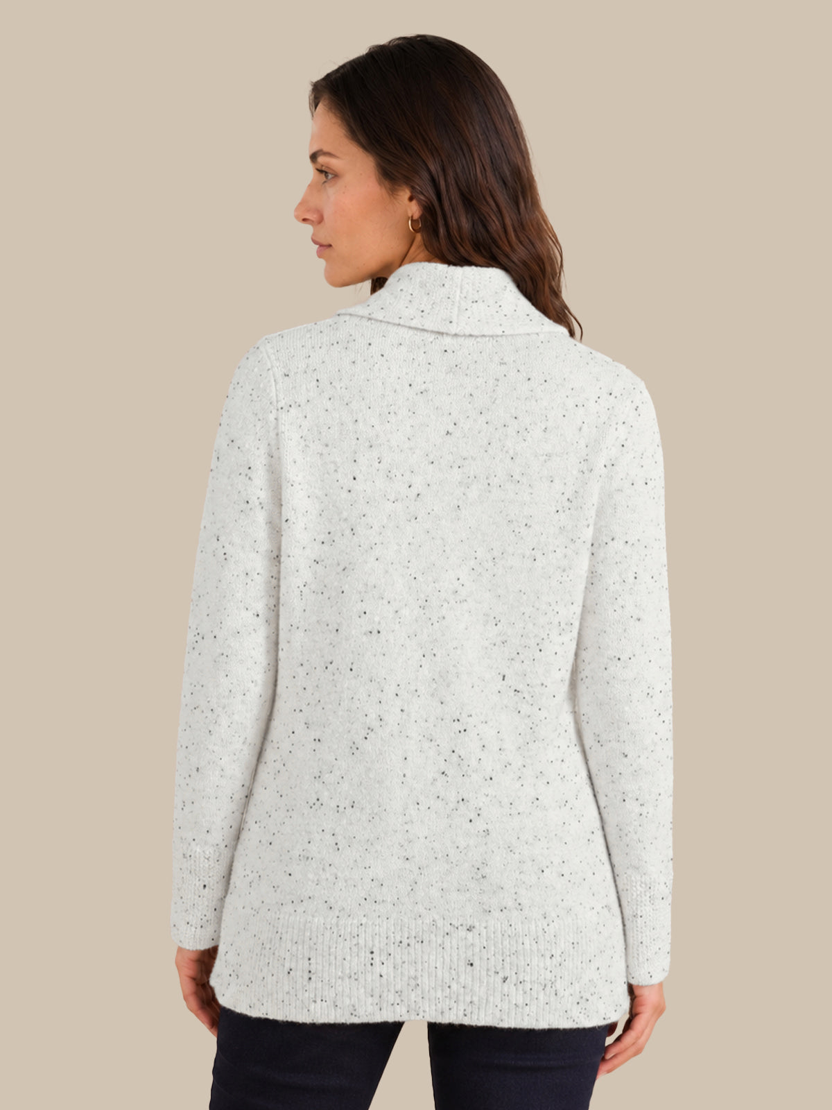 A woman shown from the back wearing a light heathered off-white knit sweater with subtle dark speckles, paired with dark pants, against a solid beige background.