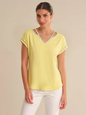 Woman wearing a yellow top with lace trim on a beige background