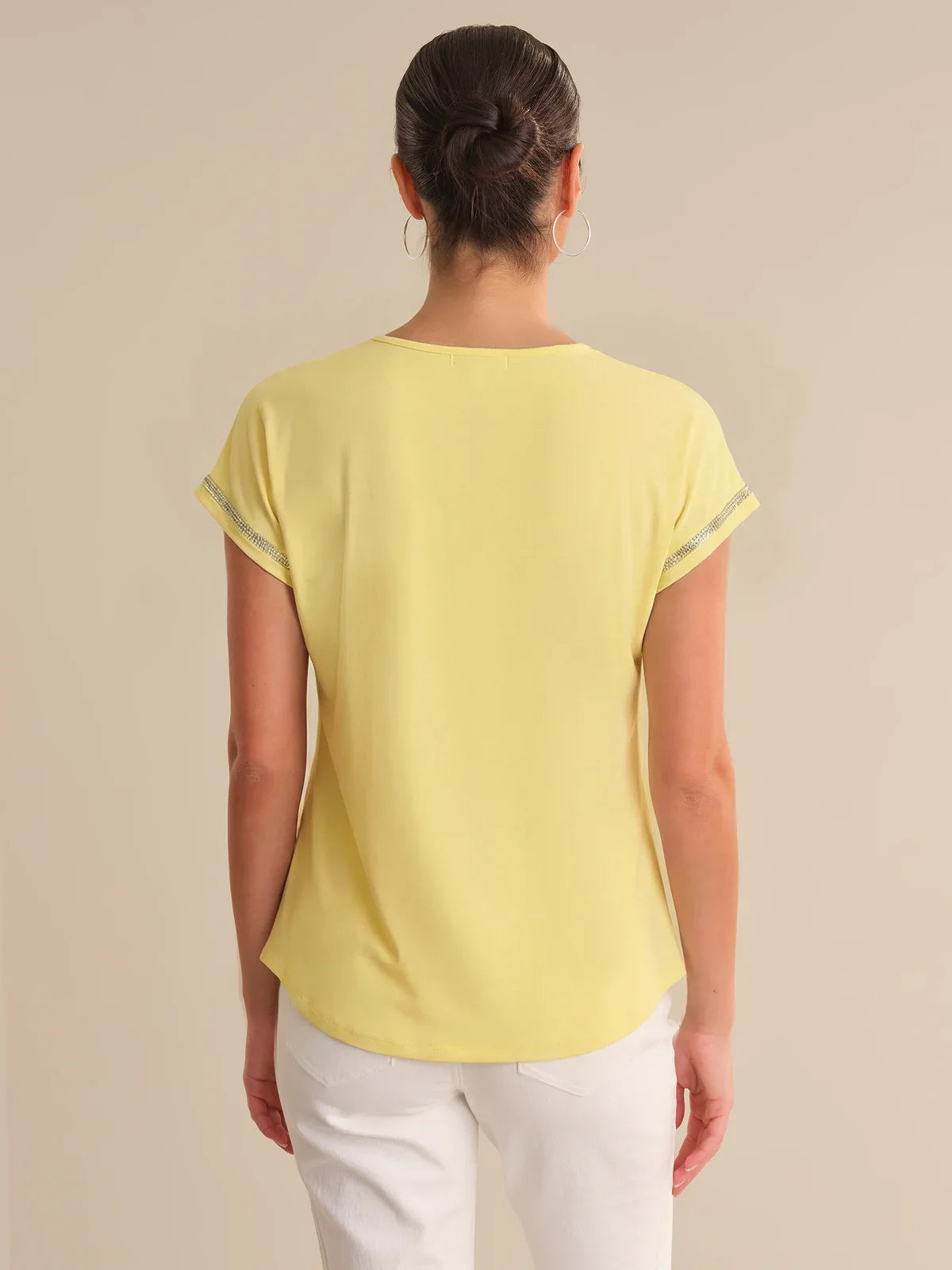 Person wearing a yellow top and white pants on a beige background