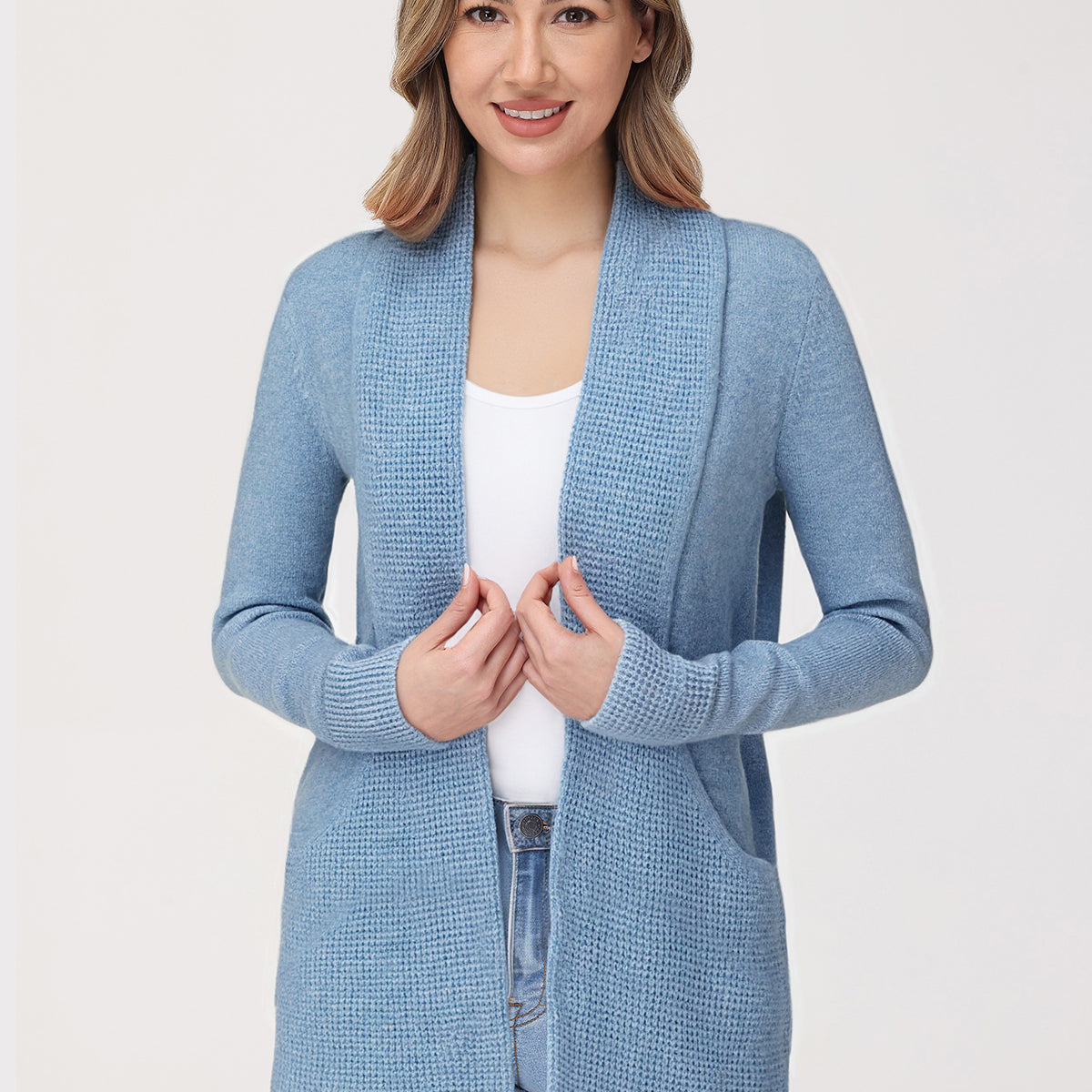 Woman wearing a light blue cardigan over a white top and jeans on a plain background