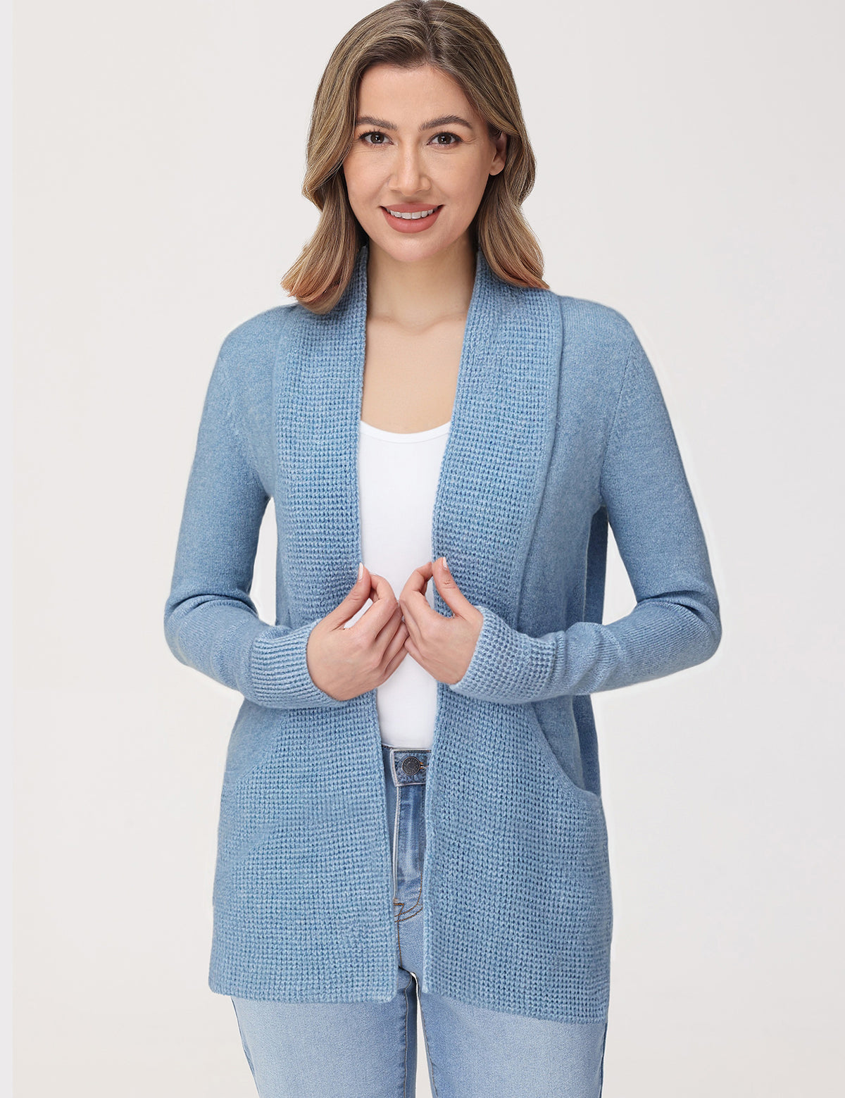 Woman wearing a light blue cardigan over a white top and jeans on a plain background