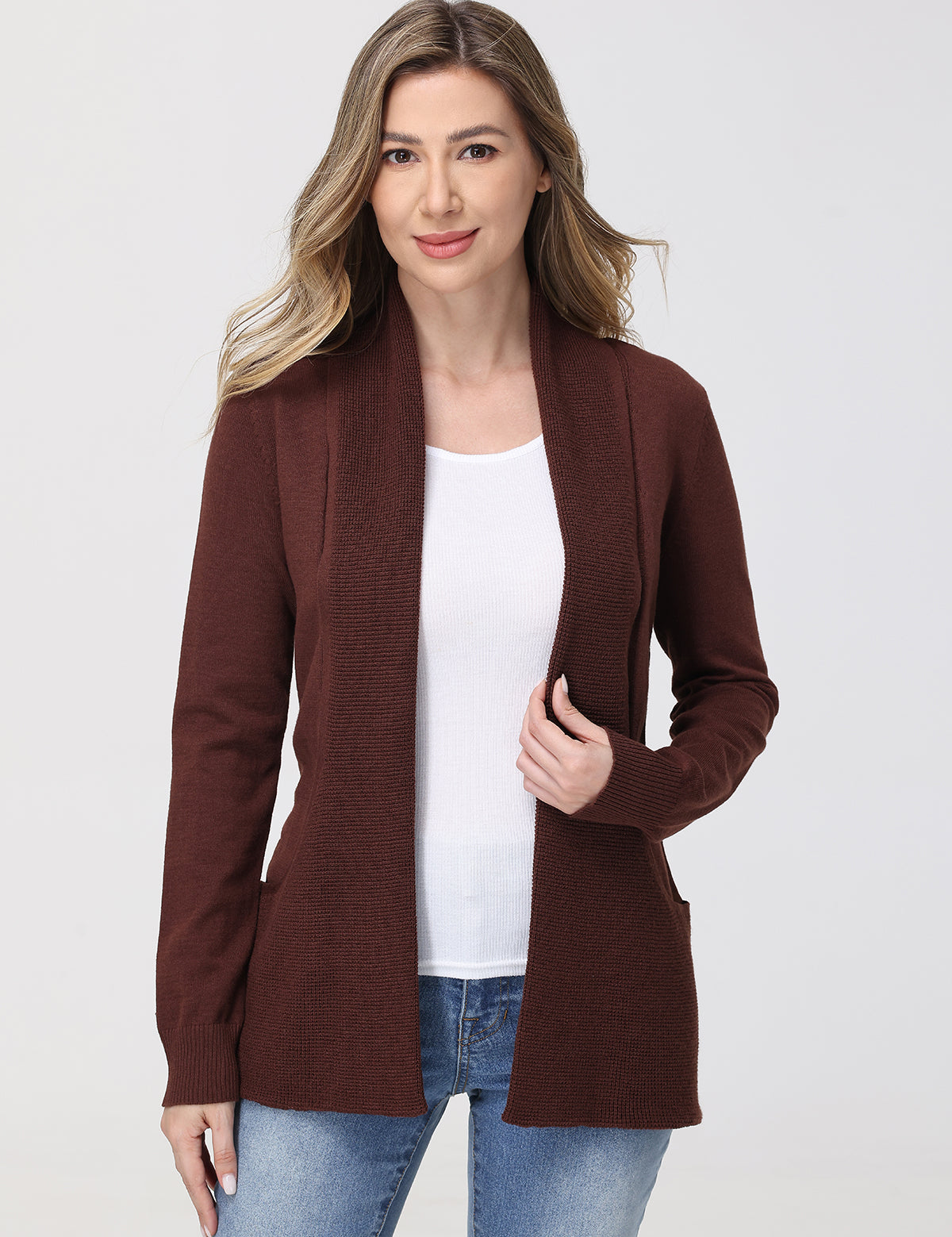 Woman wearing a brown cardigan over a white shirt and blue jeans on a white background