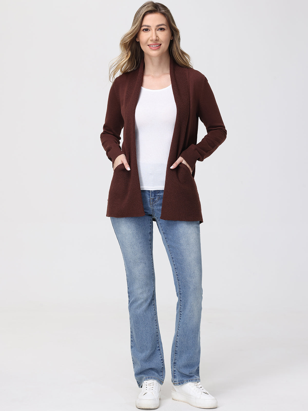 Woman wearing a brown cardigan, white shirt, blue jeans, and white sneakers on a white background