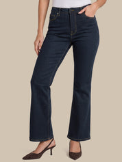 A model wearing dark blue flare jeans with a white top and brown slingback heels, shown from the waist down against a solid beige background.