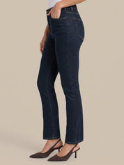 A model wearing dark blue high-waisted straight-leg jeans and dark brown slingback heels, shown from the waist down against a solid beige background.