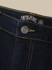 Close-up of dark indigo denim jeans showing the waistband, yellow contrast stitching, a round metal button with a Faith Jeans logo, and an interior brand label.