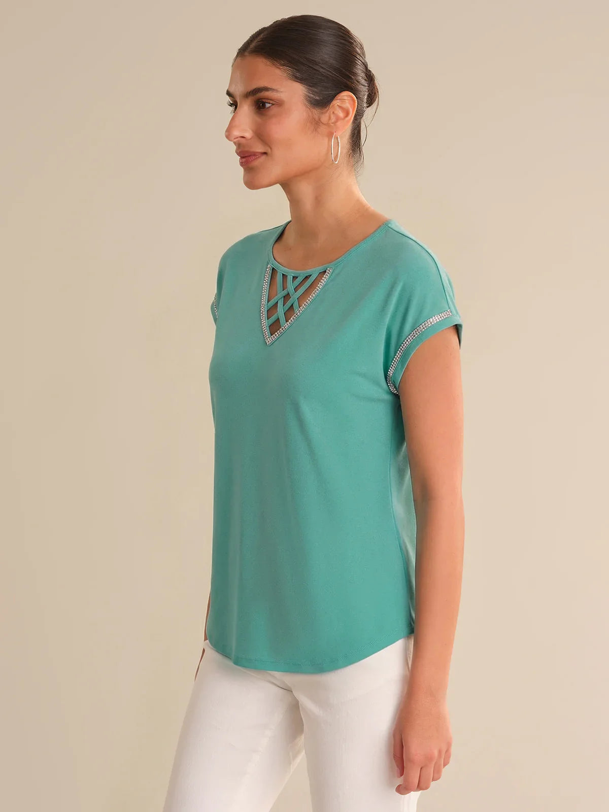 Woman wearing a teal top with a geometric neckline on a beige background