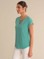 Woman wearing a teal top with a geometric neckline on a beige background