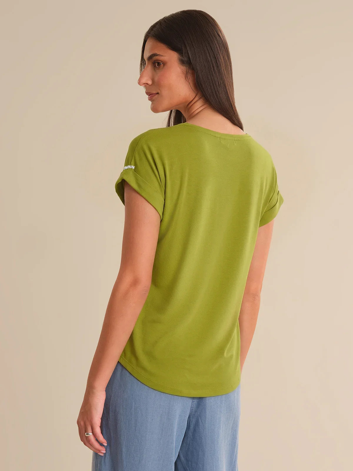 Woman wearing a green t-shirt and blue pants on a beige background