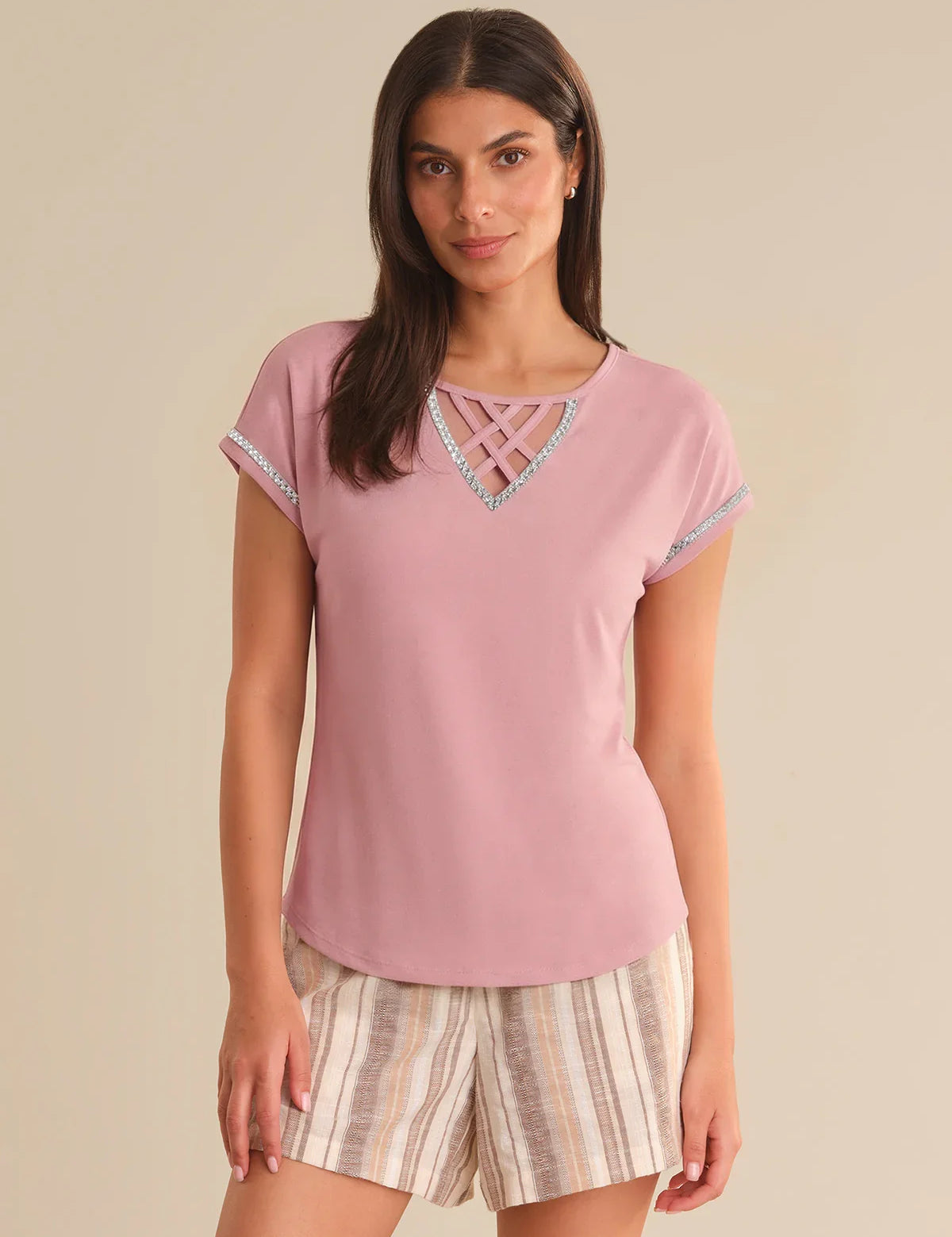 Woman wearing a pink top with lace details and striped shorts on a beige background