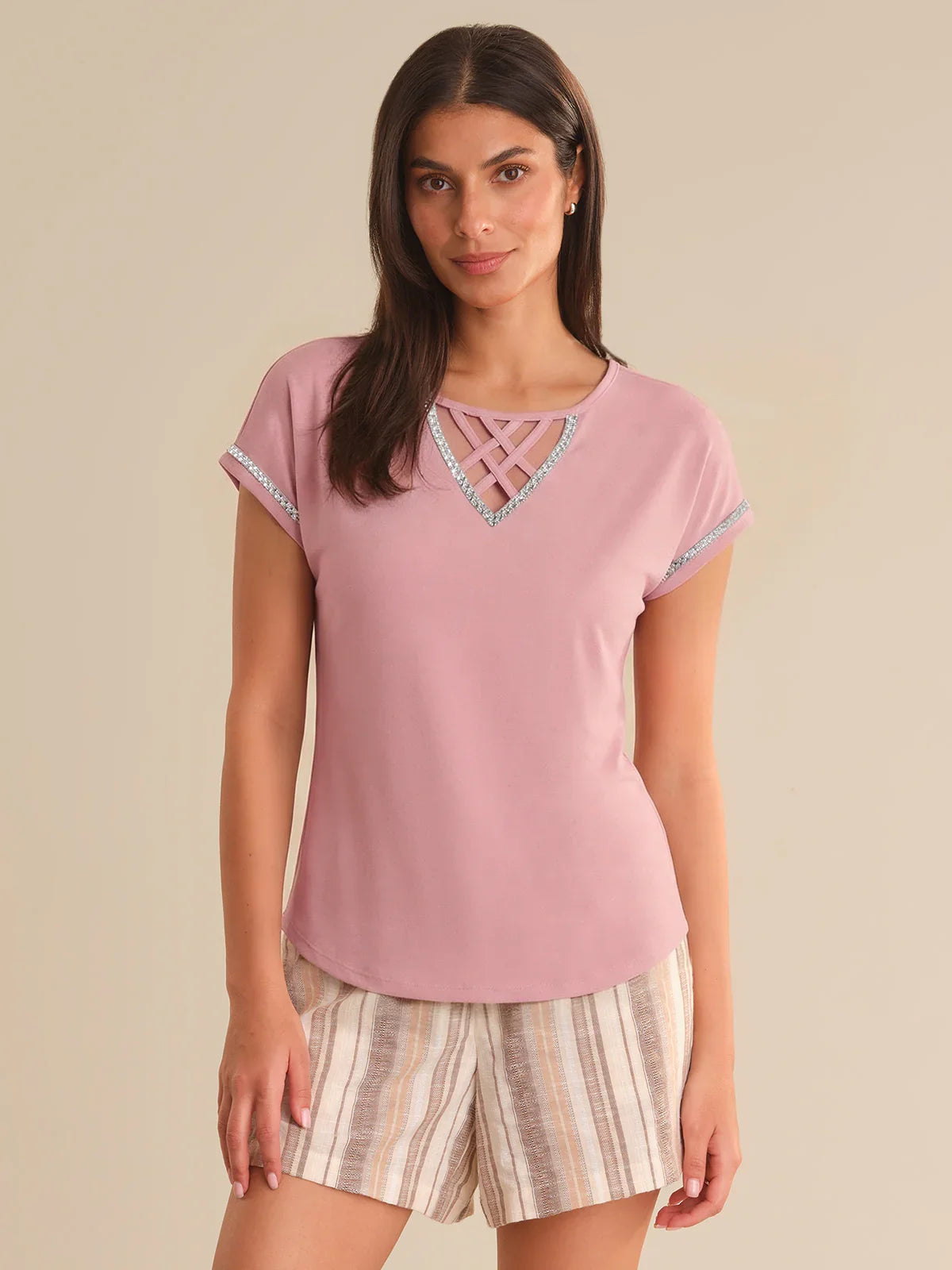 Woman wearing a pink top with lace details and striped shorts on a beige background