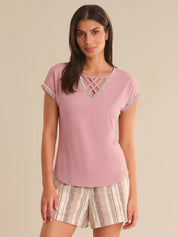 Woman wearing a pink top with lace details and striped shorts on a beige background