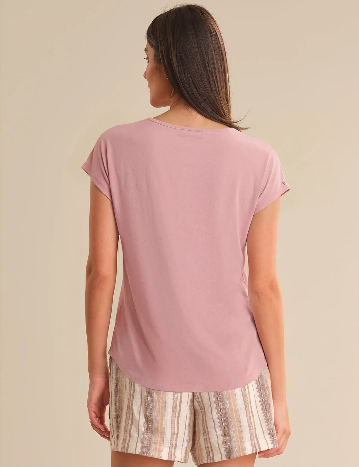 Woman wearing a pink t-shirt and patterned shorts on a beige background