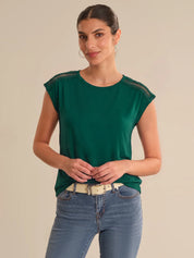 Woman wearing a green top with lace details on a beige background