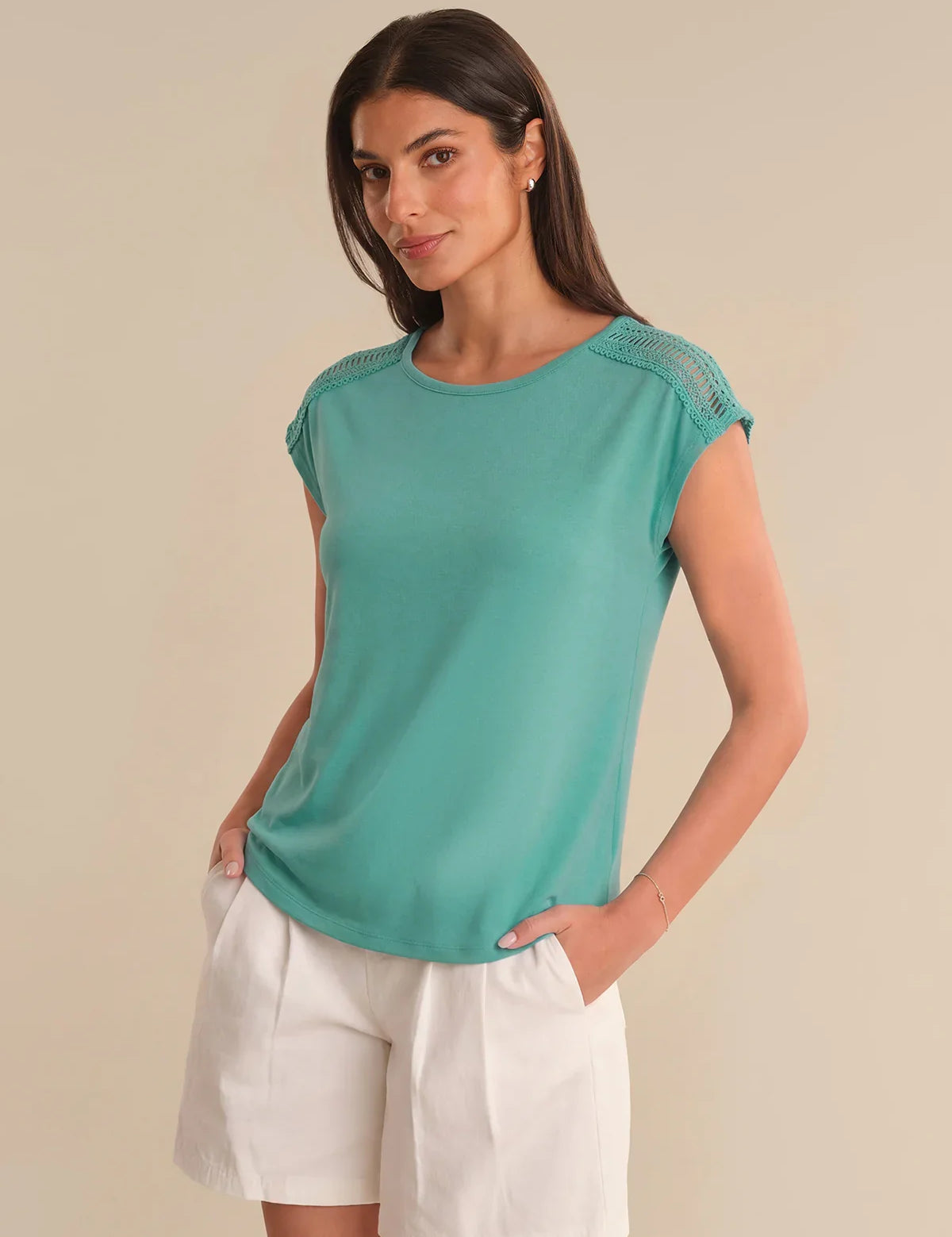 Woman wearing a teal top with white shorts on a beige background