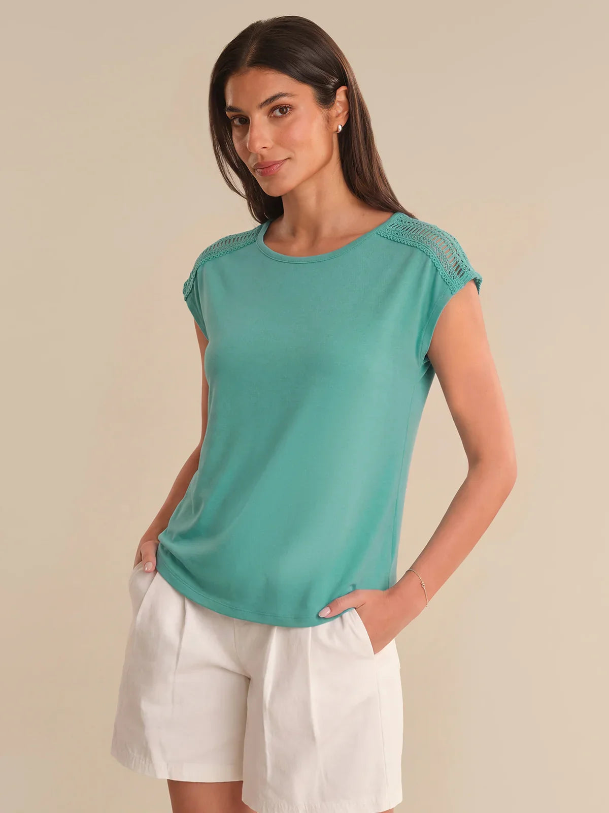 Woman wearing a teal top with white shorts on a beige background