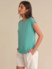 Woman wearing a teal top and white shorts on a beige background