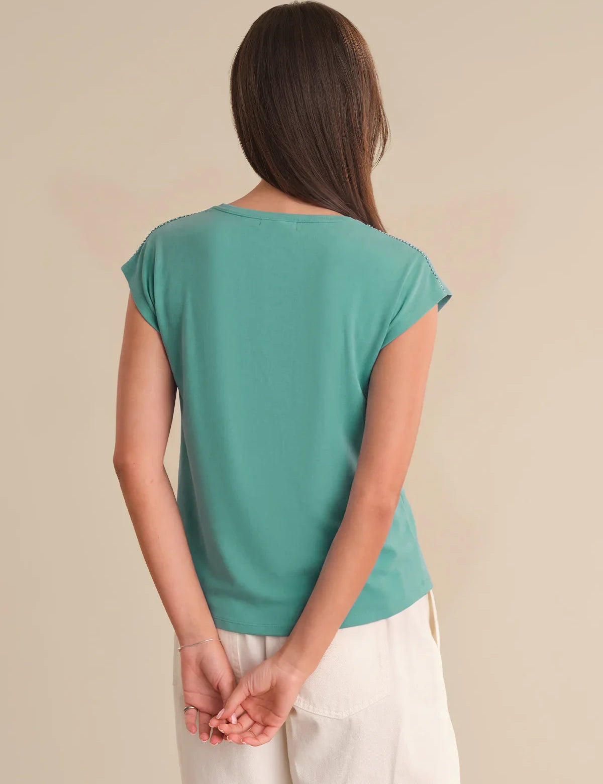 Woman wearing a teal top and white pants against a beige background