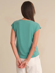 Woman wearing a teal top and white pants against a beige background