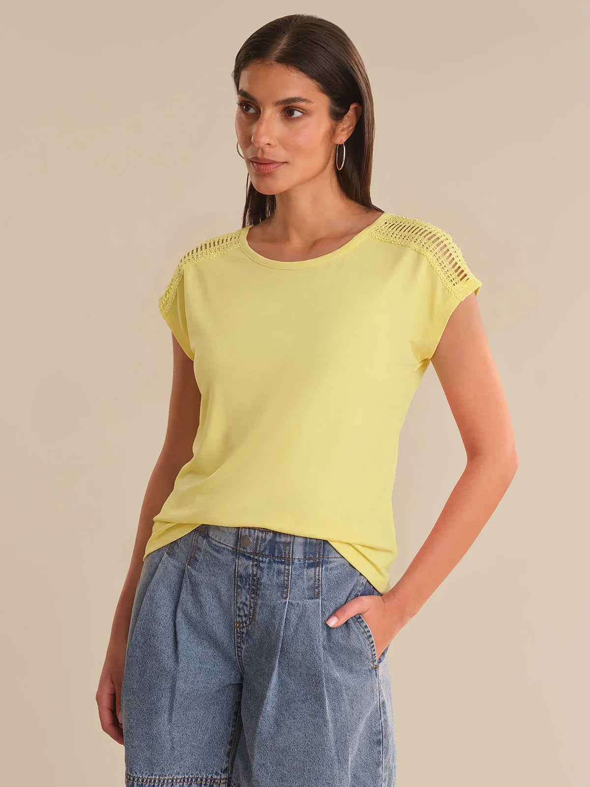 Woman wearing a yellow top and blue jeans against a beige background