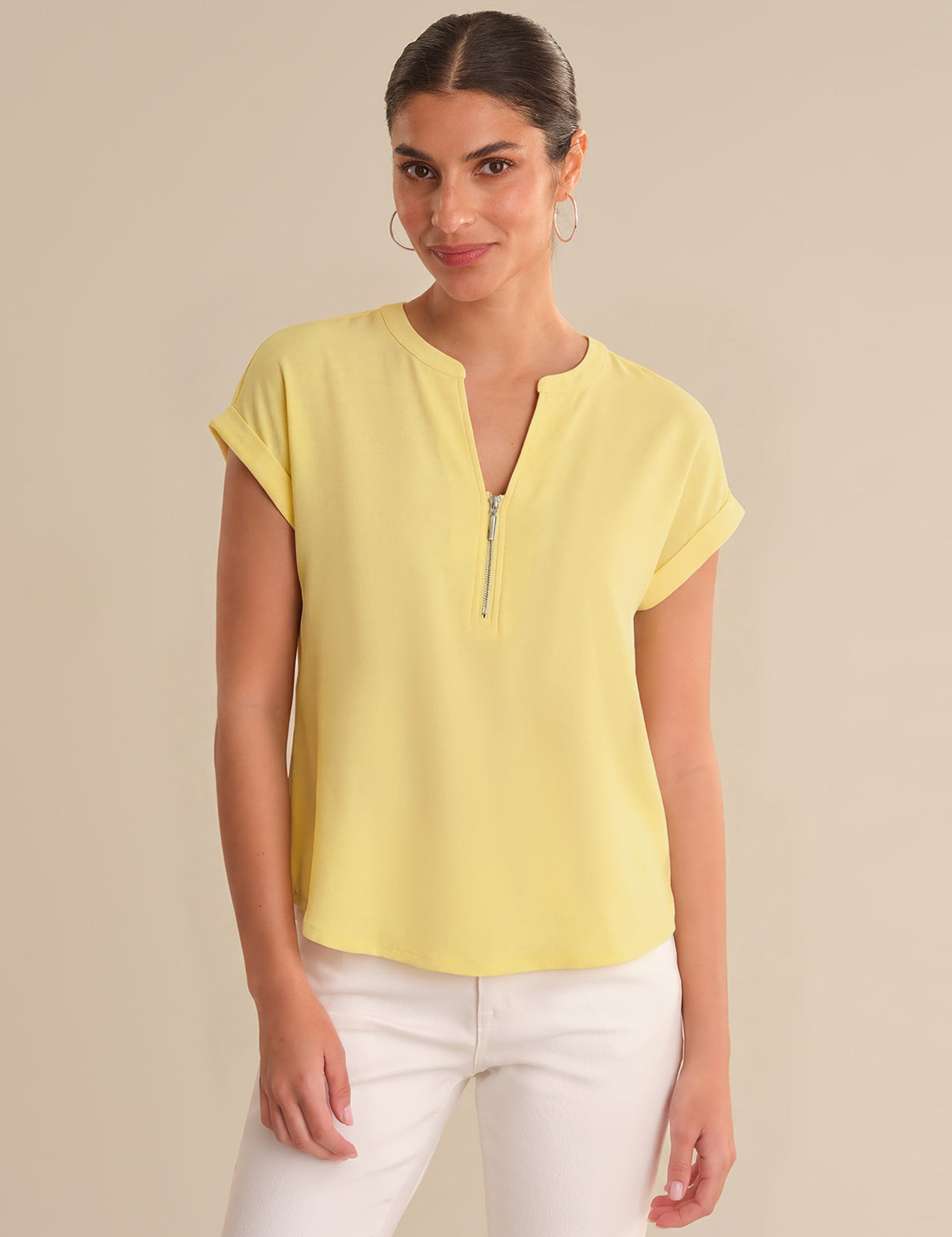 Woman wearing a yellow top with a zipper detail on a beige background