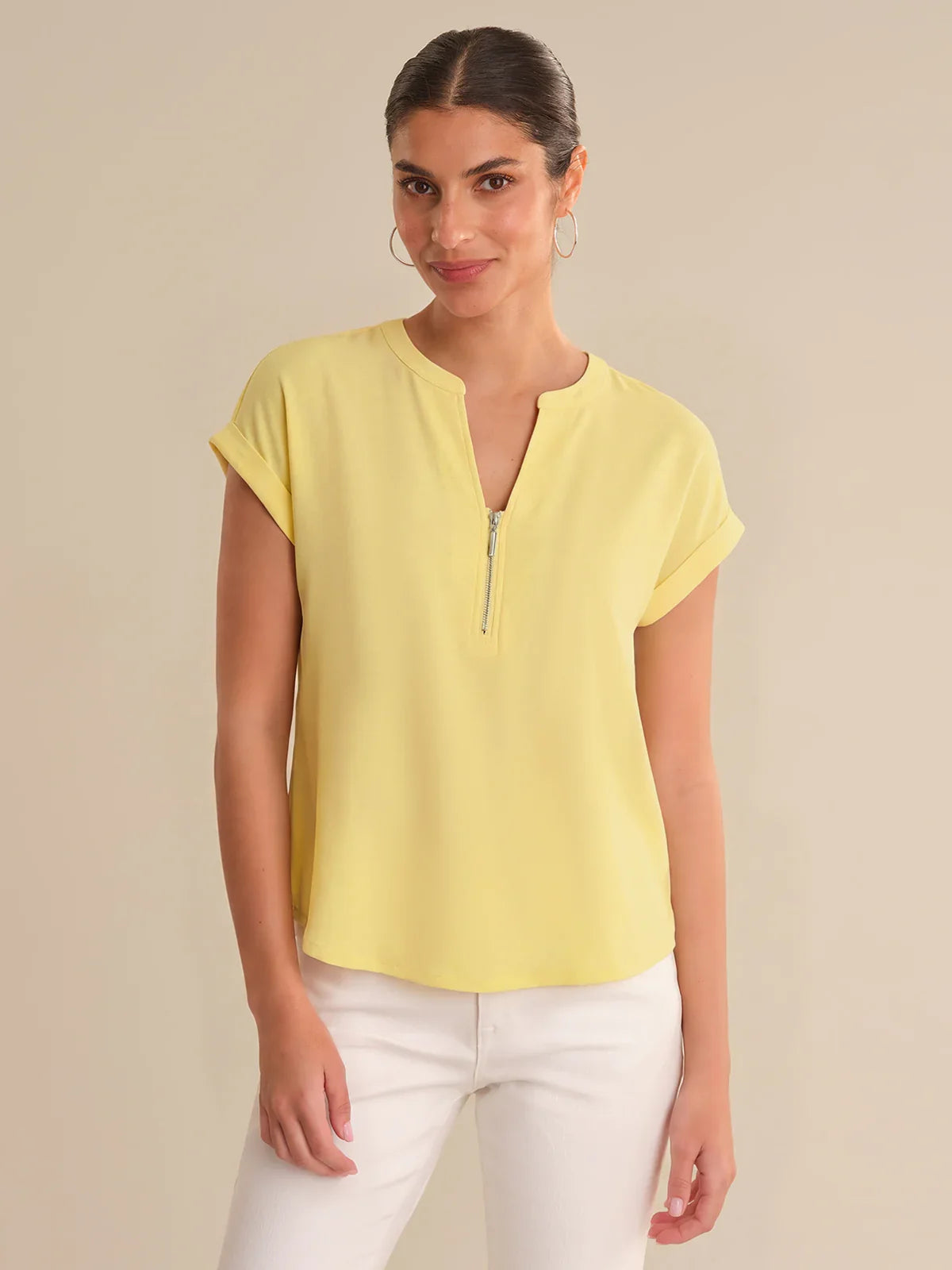 Woman wearing a yellow top with a zipper detail on a beige background
