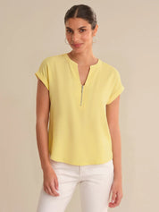 Woman wearing a yellow top with a zipper detail on a beige background