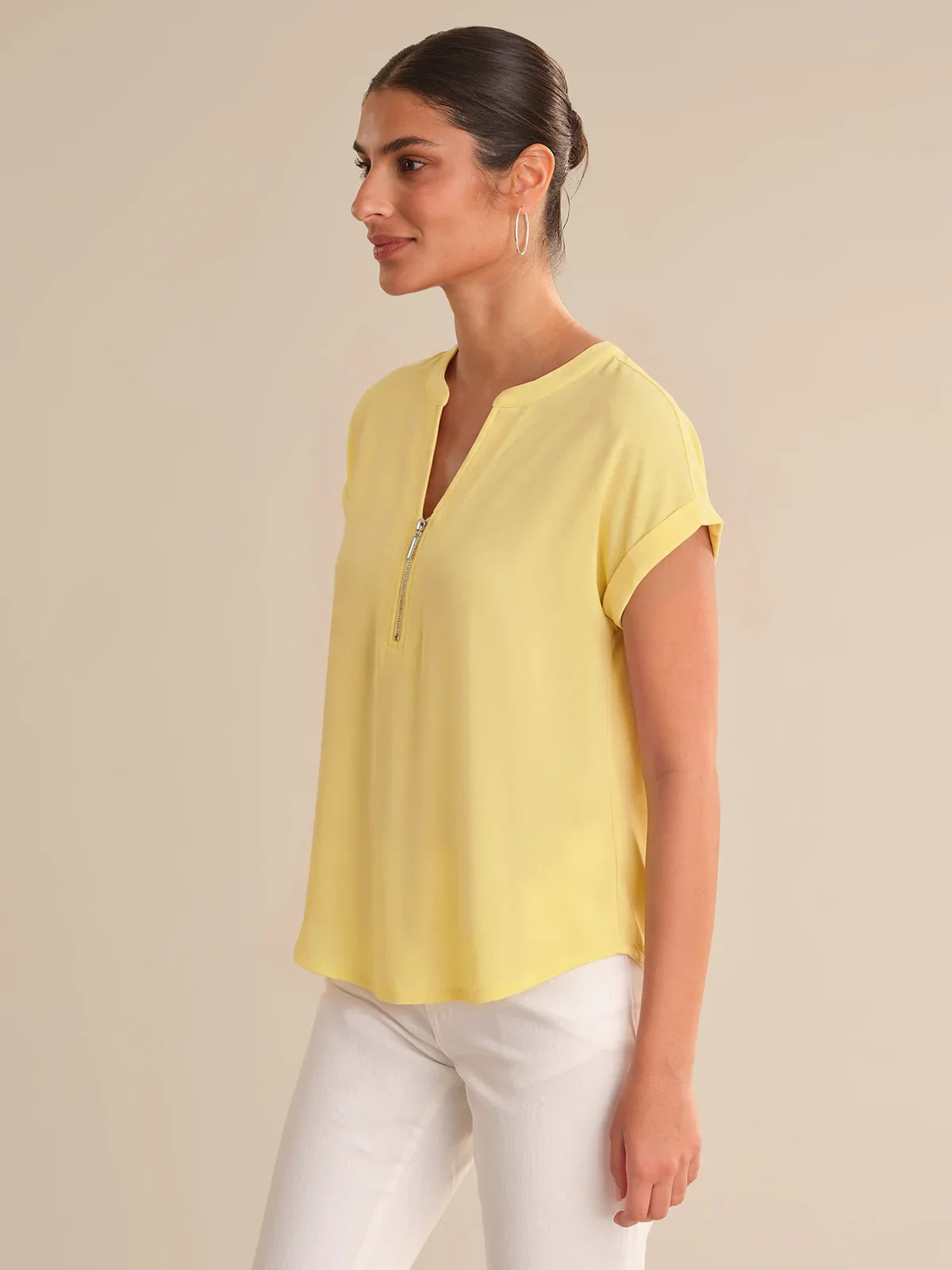 Woman wearing a yellow top and white pants against a beige background