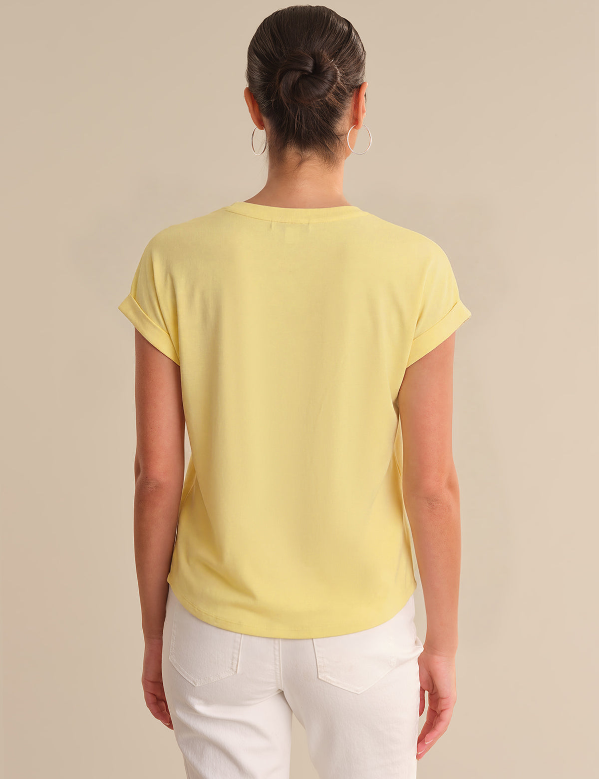 Person wearing a yellow t-shirt and white pants on a beige background