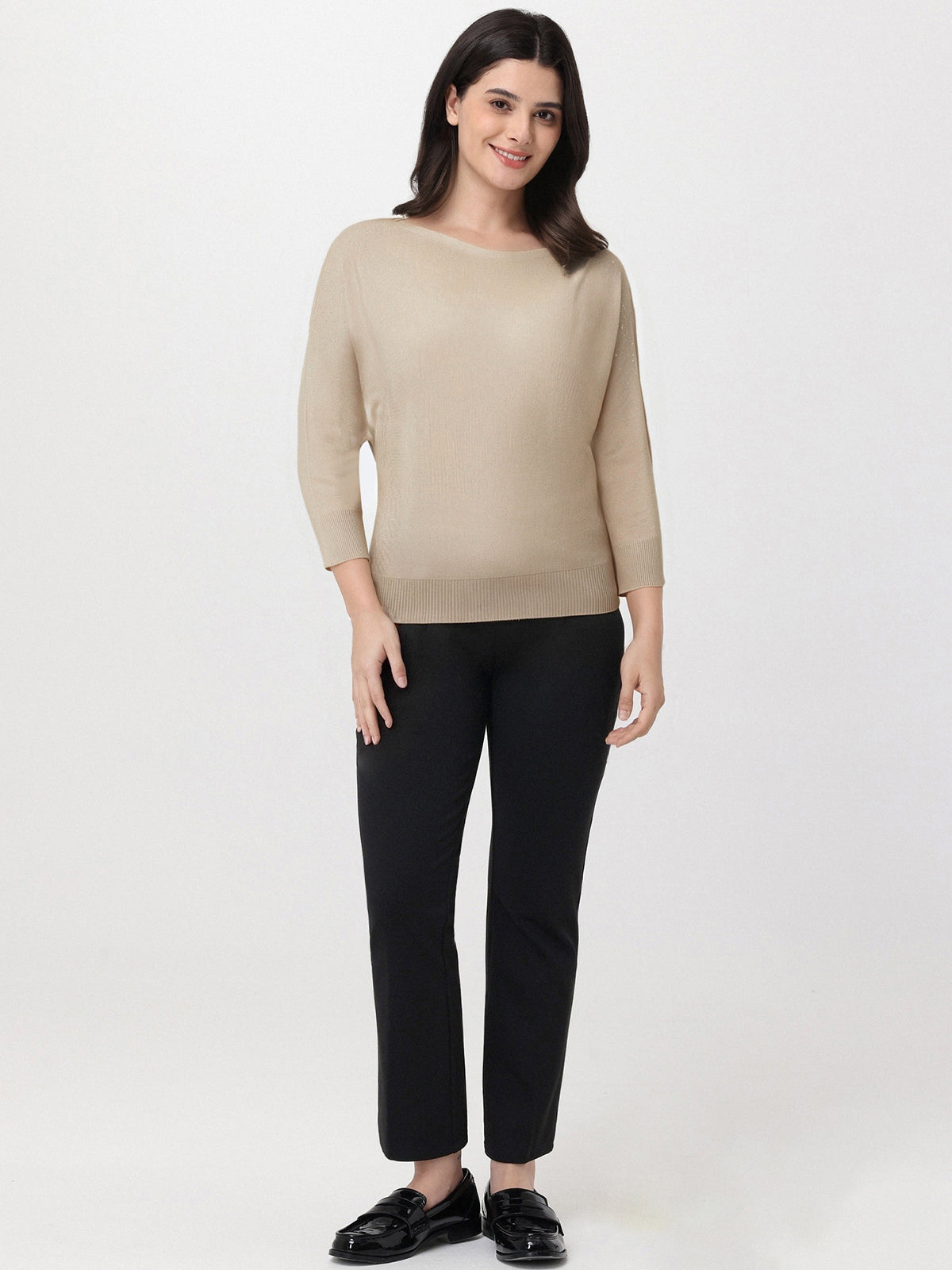 Woman wearing a beige sweater and black pants on a white background