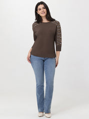 Woman wearing a brown top with studded shoulders and blue jeans on a white background