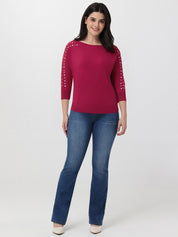 Woman wearing a red sweater with grommet sleeves and blue jeans on a white background