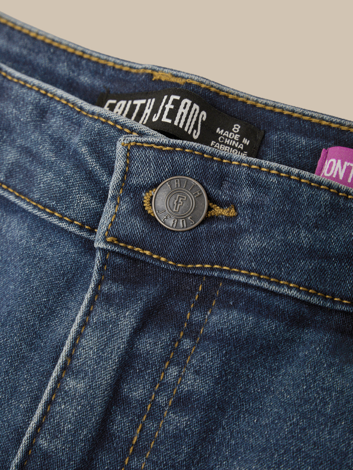 Close-up of a pair of blue denim jeans showing the waistband, button closure, and inner label reading FAITHJEANS.