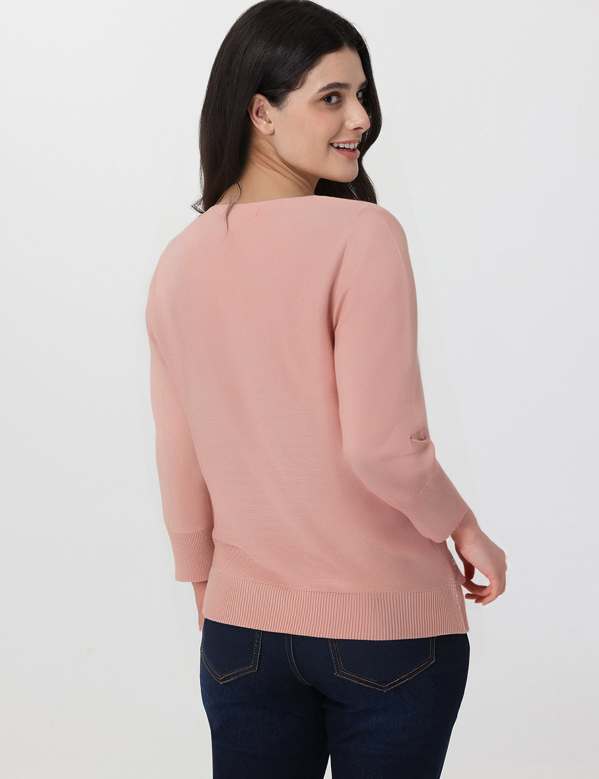Woman wearing a pink sweater and dark jeans on a white background