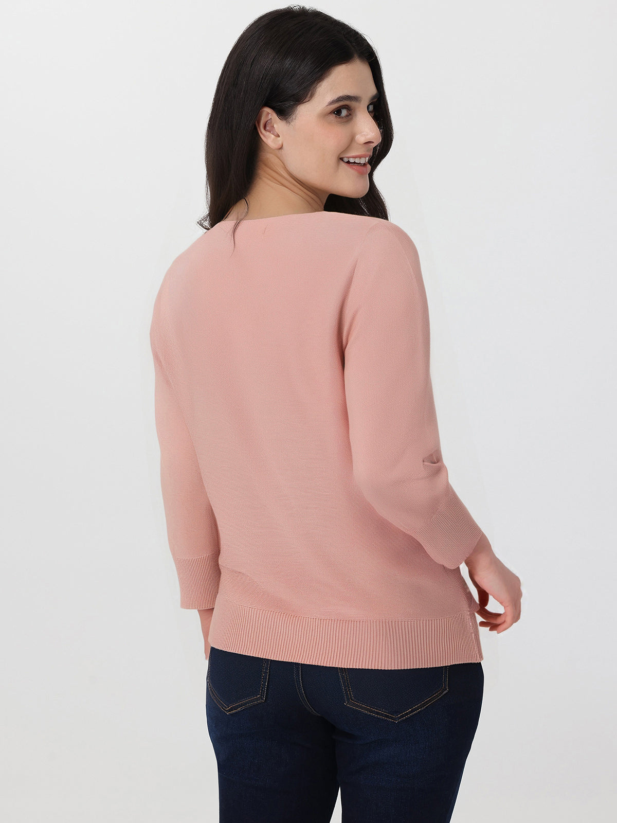 Woman wearing a pink sweater and dark jeans on a white background