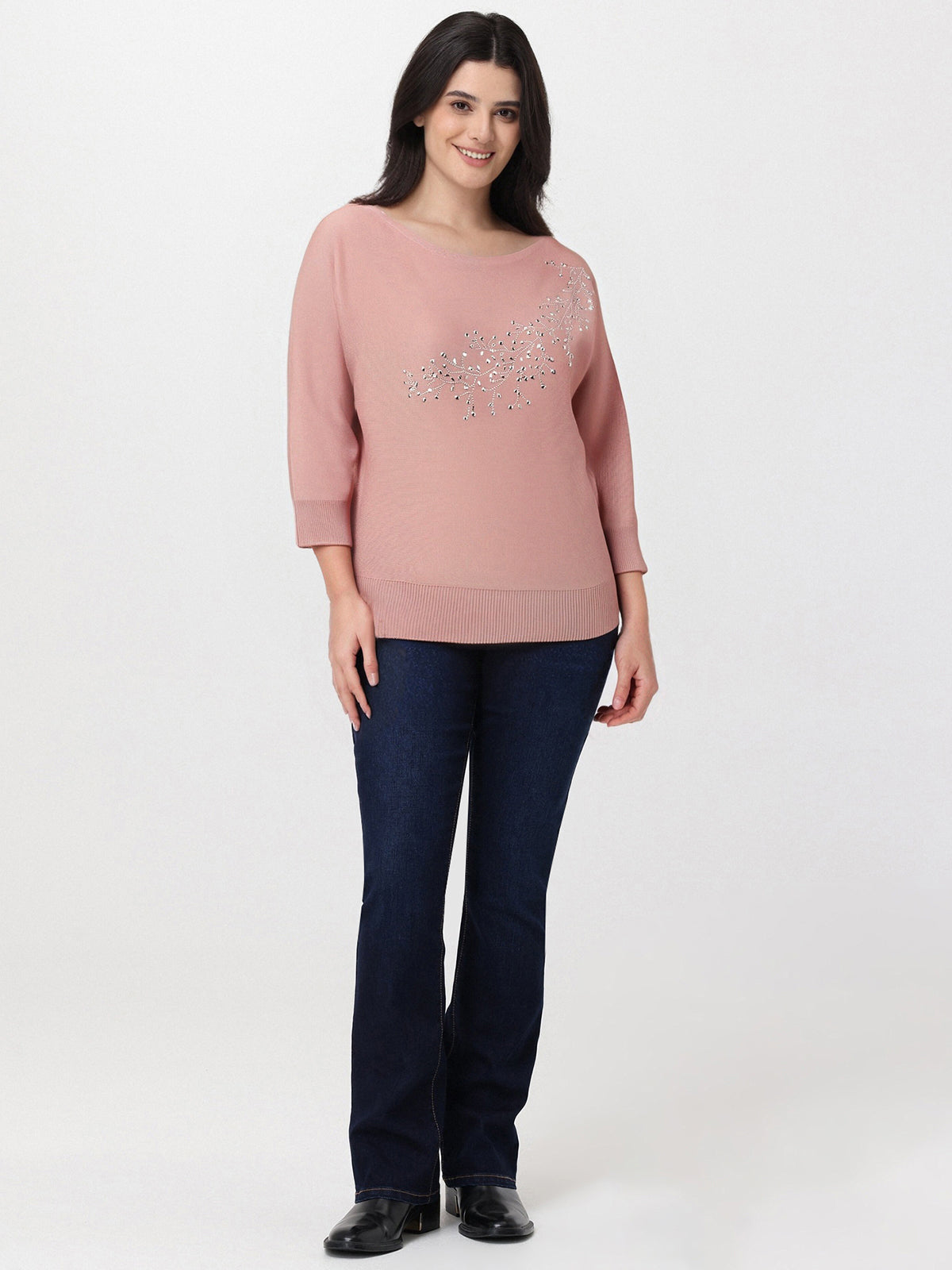 Woman wearing a pink sweater with a decorative element and dark blue jeans on a white background