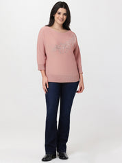 Woman wearing a pink sweater with a decorative element and dark blue jeans on a white background