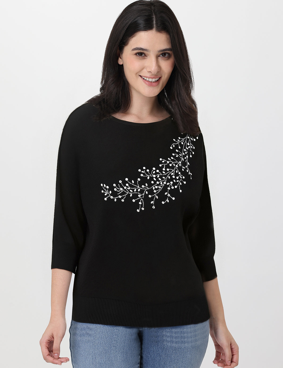 Woman wearing a black sweater with white rhinestone embroidery on a plain background