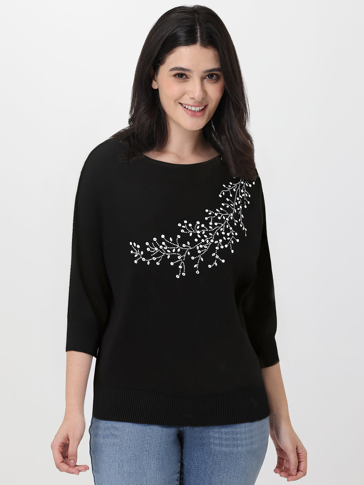 Woman wearing a black sweater with white rhinestone embroidery on a plain background