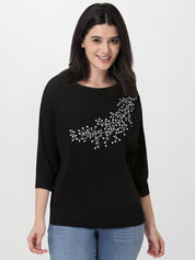 Woman wearing a black sweater with white rhinestone embroidery on a plain background